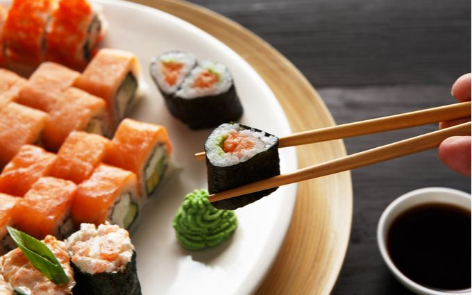 箸を使って巻きずしを食べようとしている画像