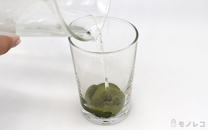 コップに入ったサントリーウエルネス 極の青汁の粉末に水を注いでいるシーンの画像