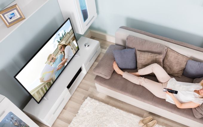 リビングでソファに横たわった女性がテレビを見ている画像